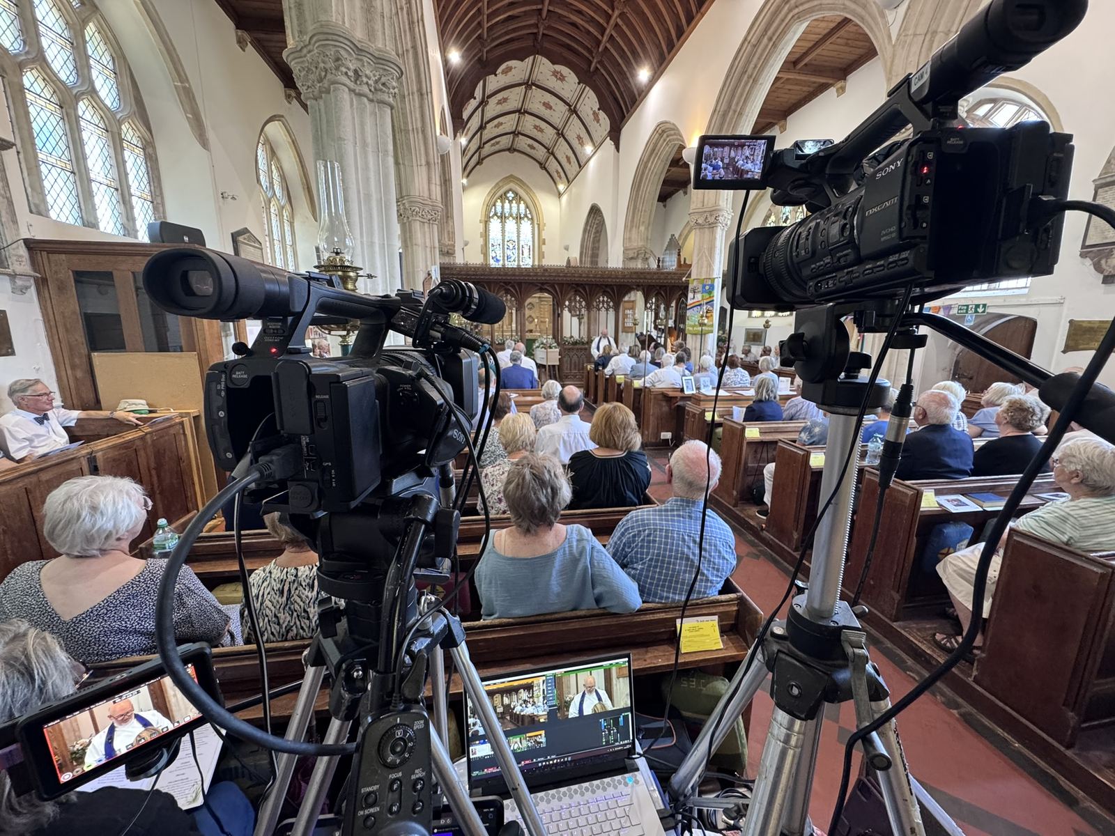 Two cameras set up at the back of a church during a wedding service