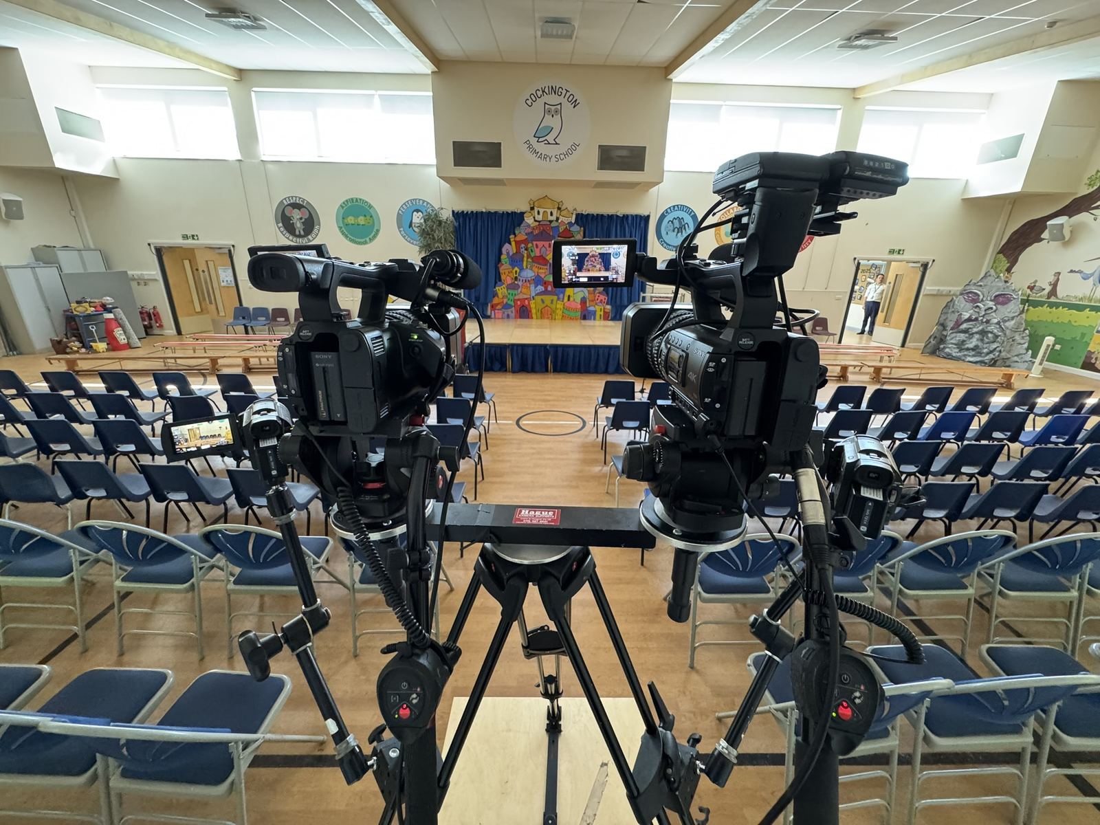 Two camcorders on a shared rig facing a primary school stage
